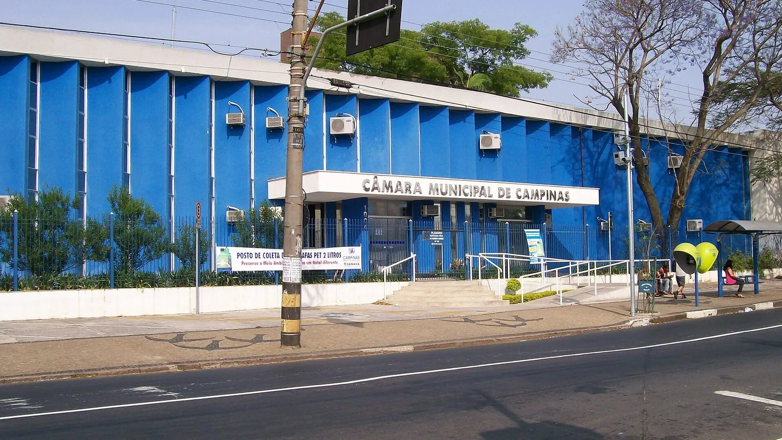 Fachada azul da Câmara Municipal de Campinas, com o nome do prédio sobre a entrada, vista da rua