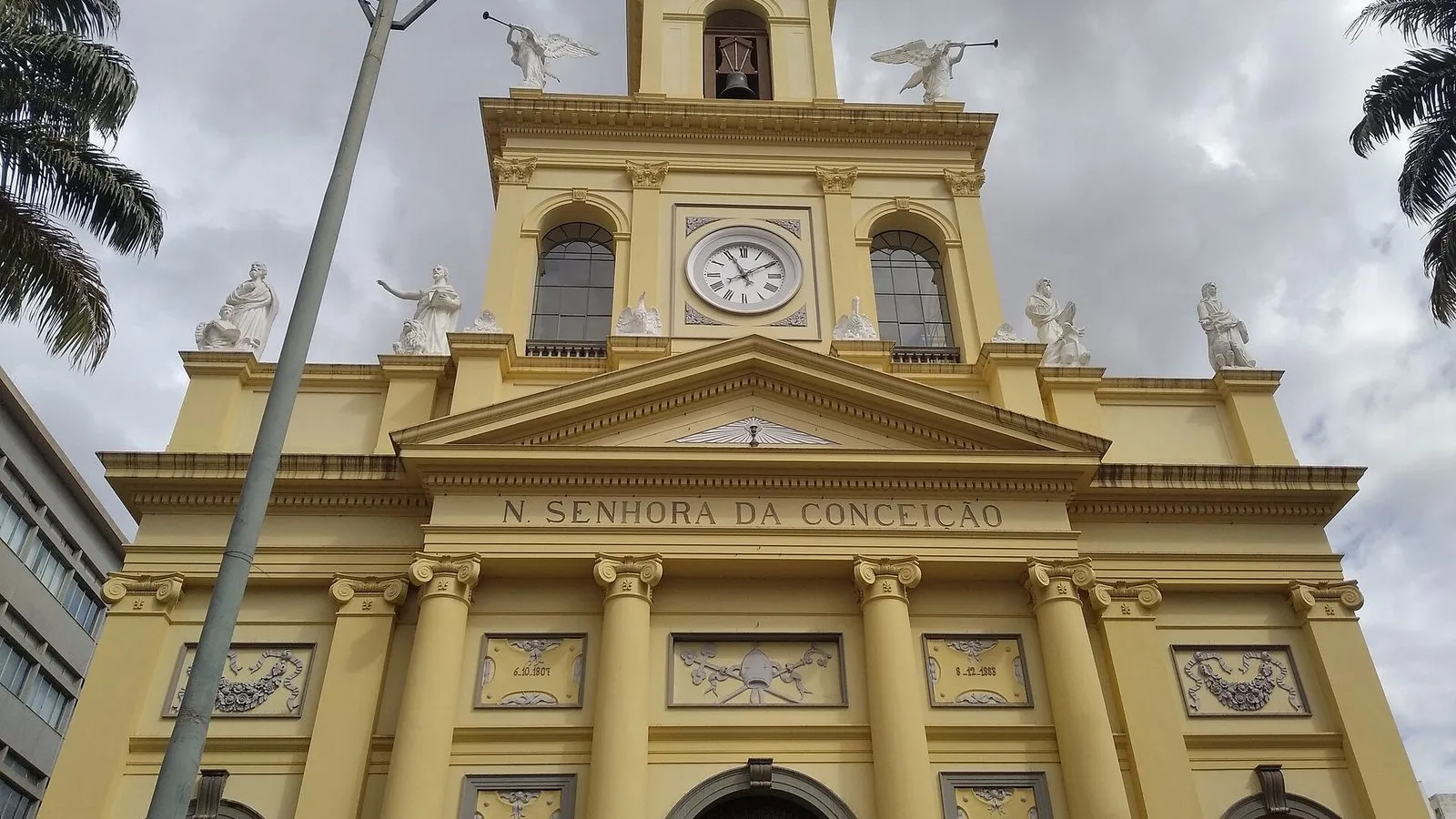 Fachada amarela da Catedral Metropolitana de Campinas, com relógio, sino, estátuas no alto e as datas de 1807 e 1883 em medalhões
