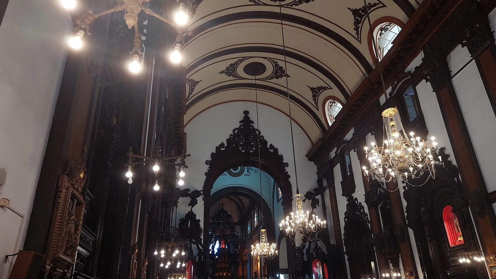 Nave da Catedral Metropolitana de Campinas, com teto em abóbada, lustres acesos e paredes cobertas de talha escura em madeira