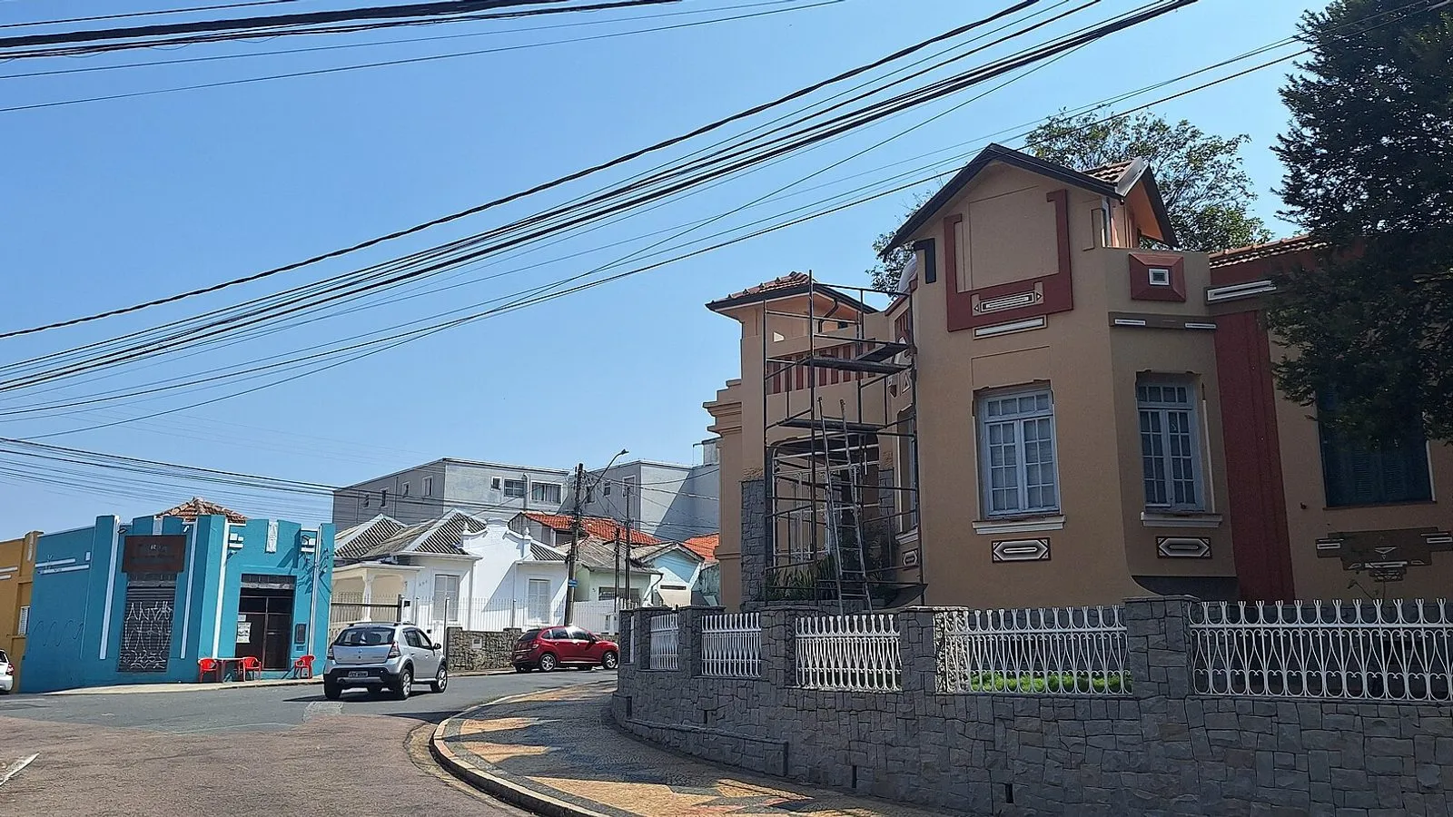 Esquina da Vila Industrial, em Campinas, com casarão antigo de fachada ocre e detalhes vermelhos, gradil branco e casas baixas coloridas ao fundo