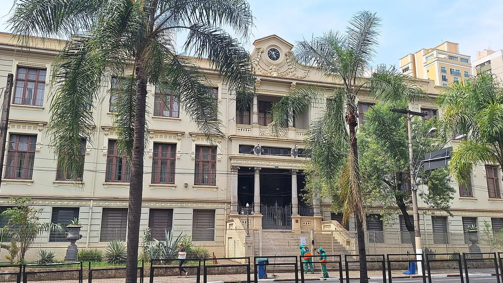Fachada histórica da Escola Estadual Carlos Gomes, em Campinas, com relógio no alto e palmeiras na calçada