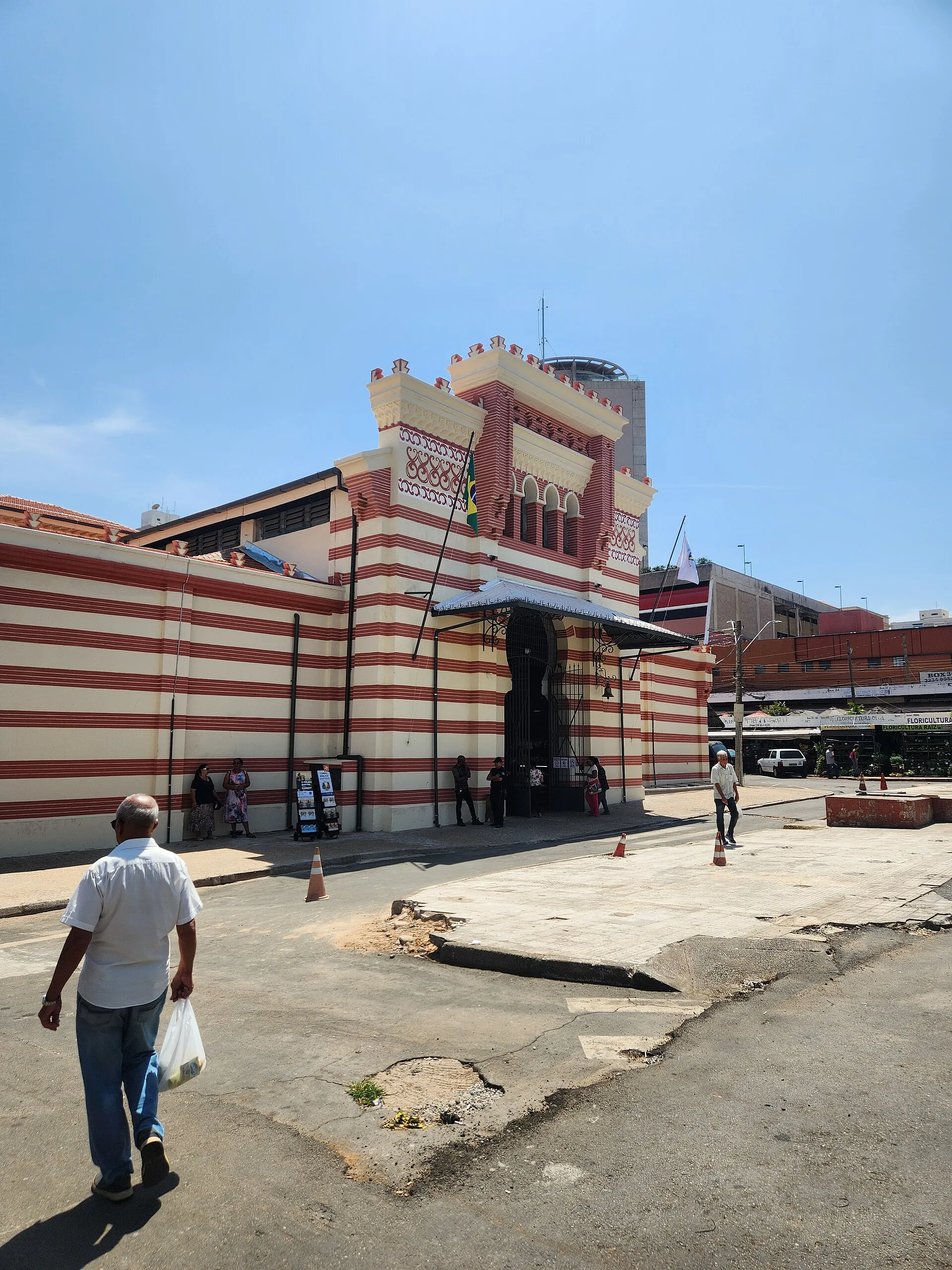 Fachada do Mercado Municipal de Campinas com arquitetura de tijolos vermelhos e brancos, sob céu azul claro.