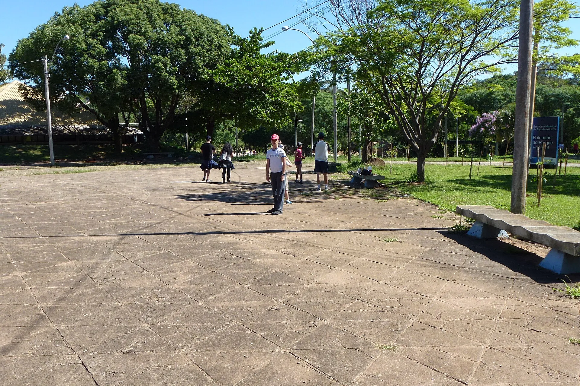 Parque Taquaral com áreas verdes, árvores e piso de concreto em dia ensolarado