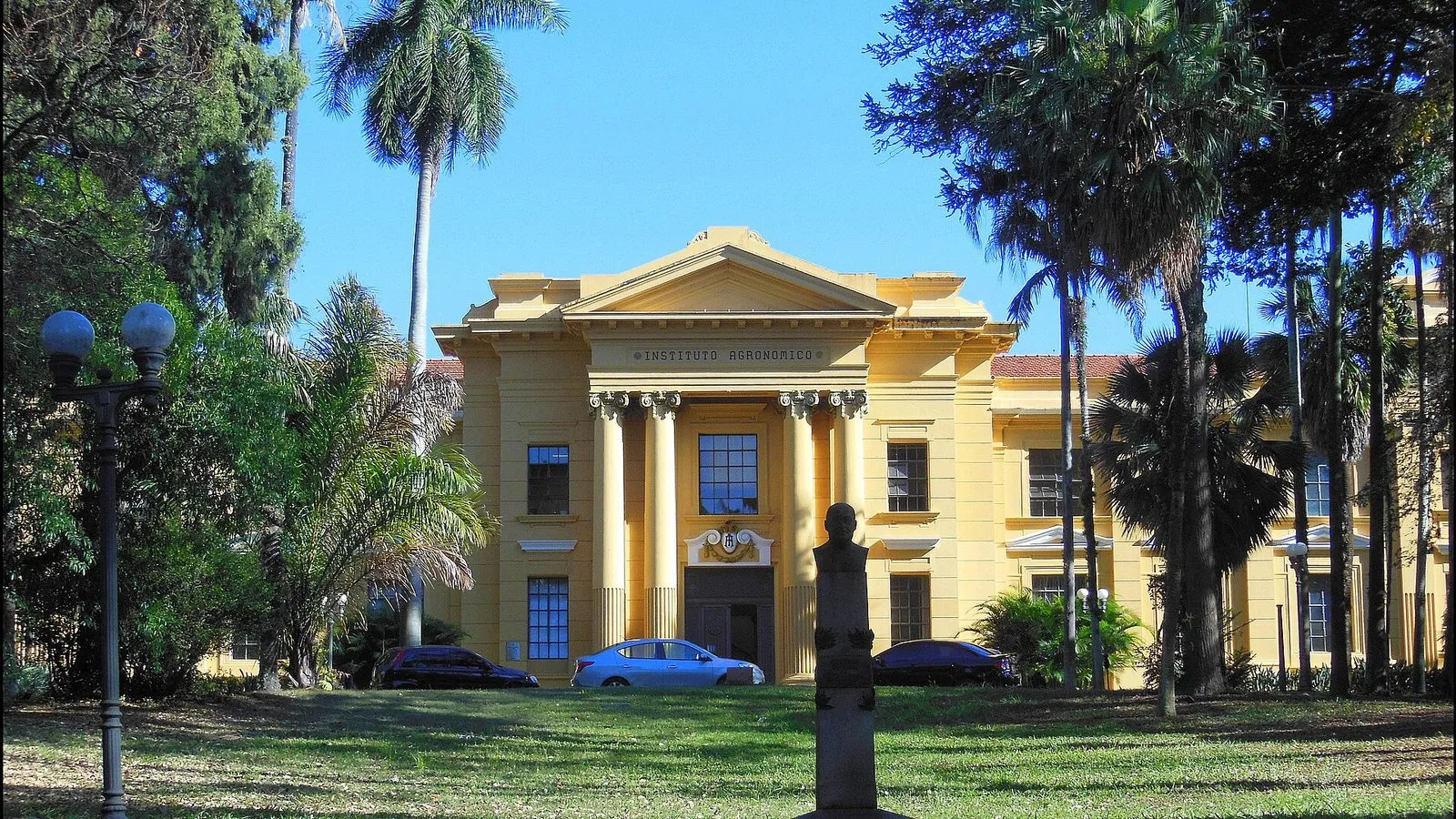 Prédio histórico amarelo do Instituto Agronômico, com colunas na fachada, cercado de palmeiras e gramado, na Avenida Barão de Itapura, em Campinas