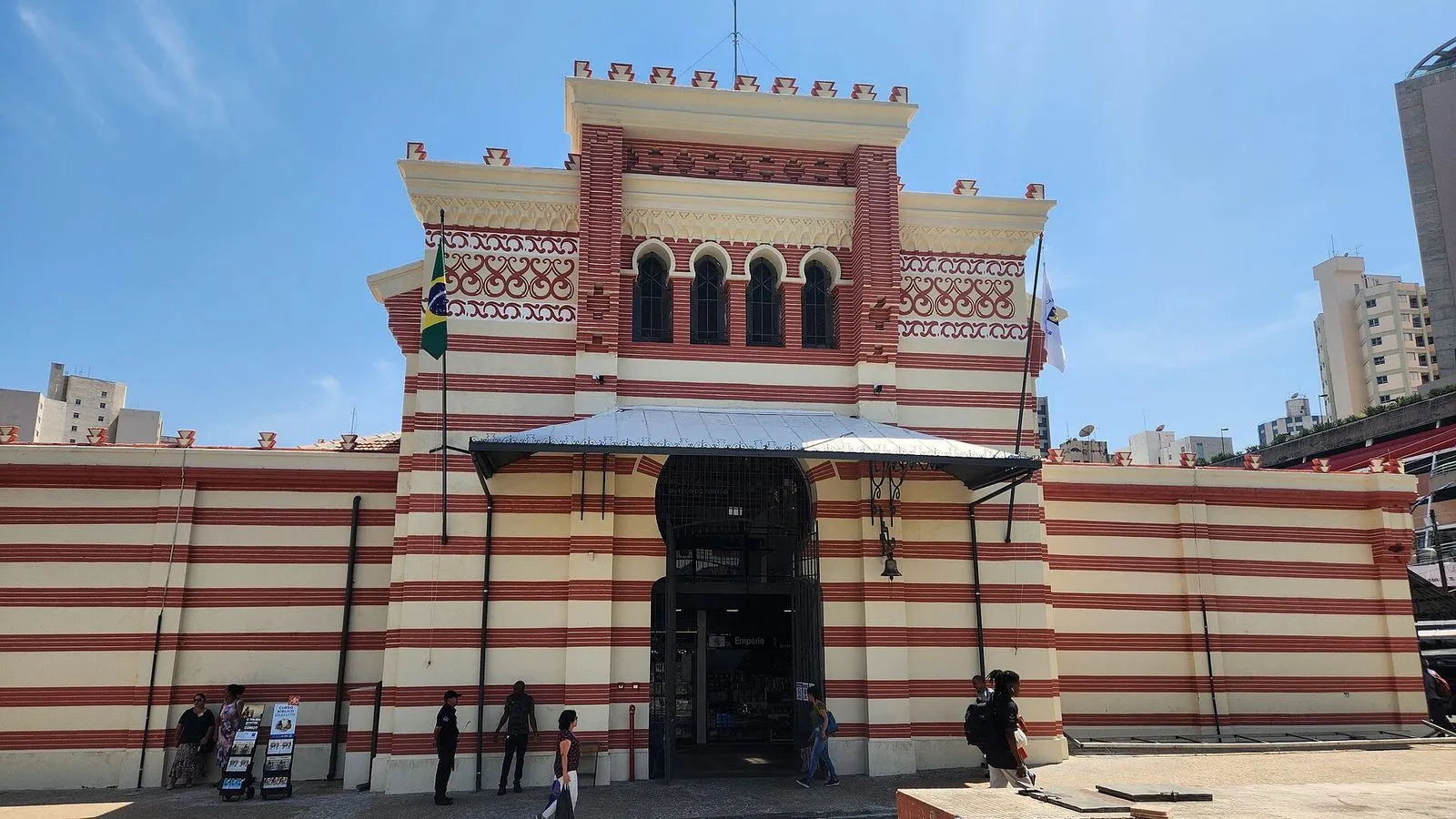 Fachada listrada em creme e vermelho do Mercado Municipal de Campinas, com a entrada principal, em dia de sol