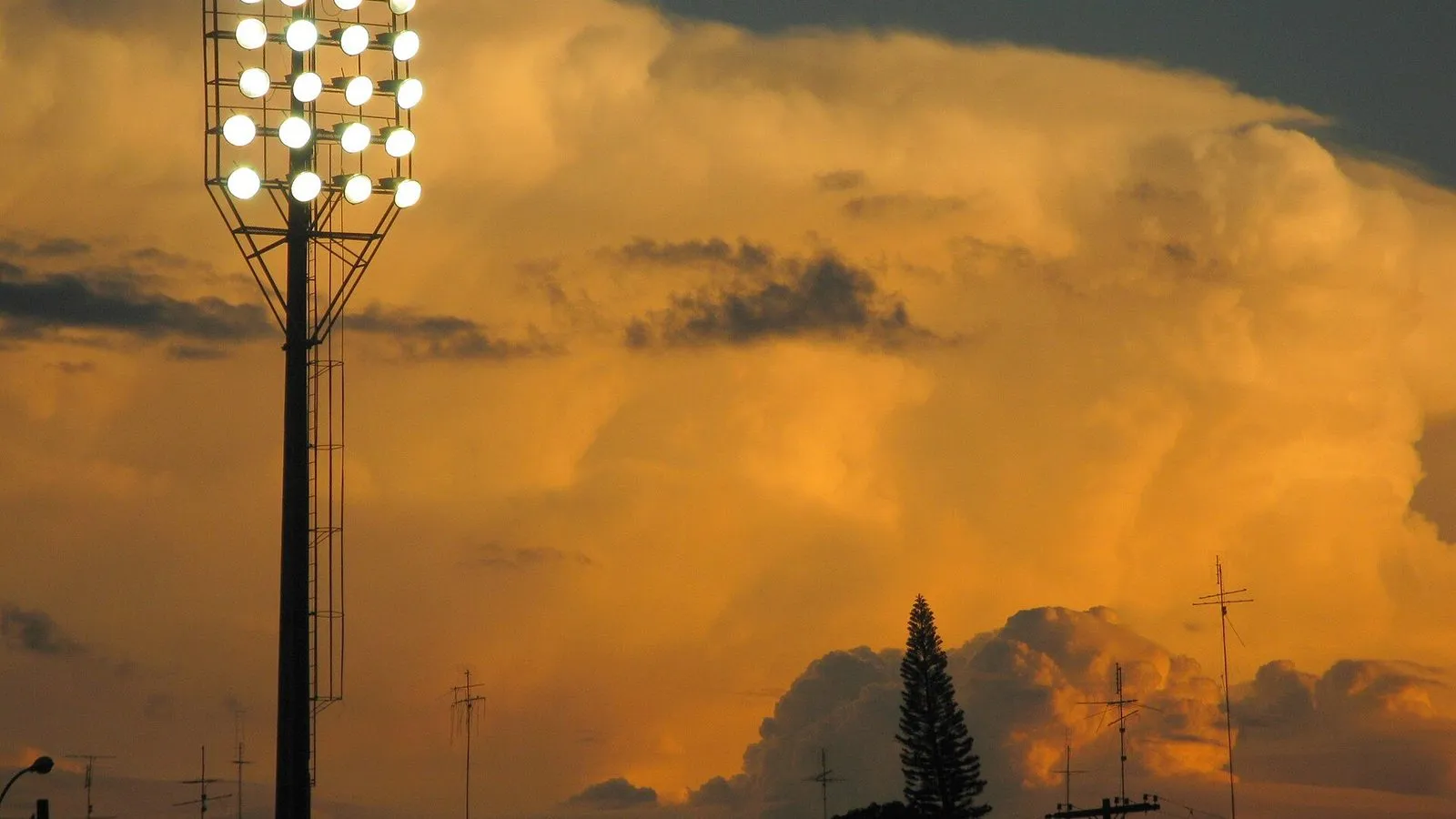 Torre de refletores do Estádio Moisés Lucarelli acesa, com nuvens alaranjadas ao fundo