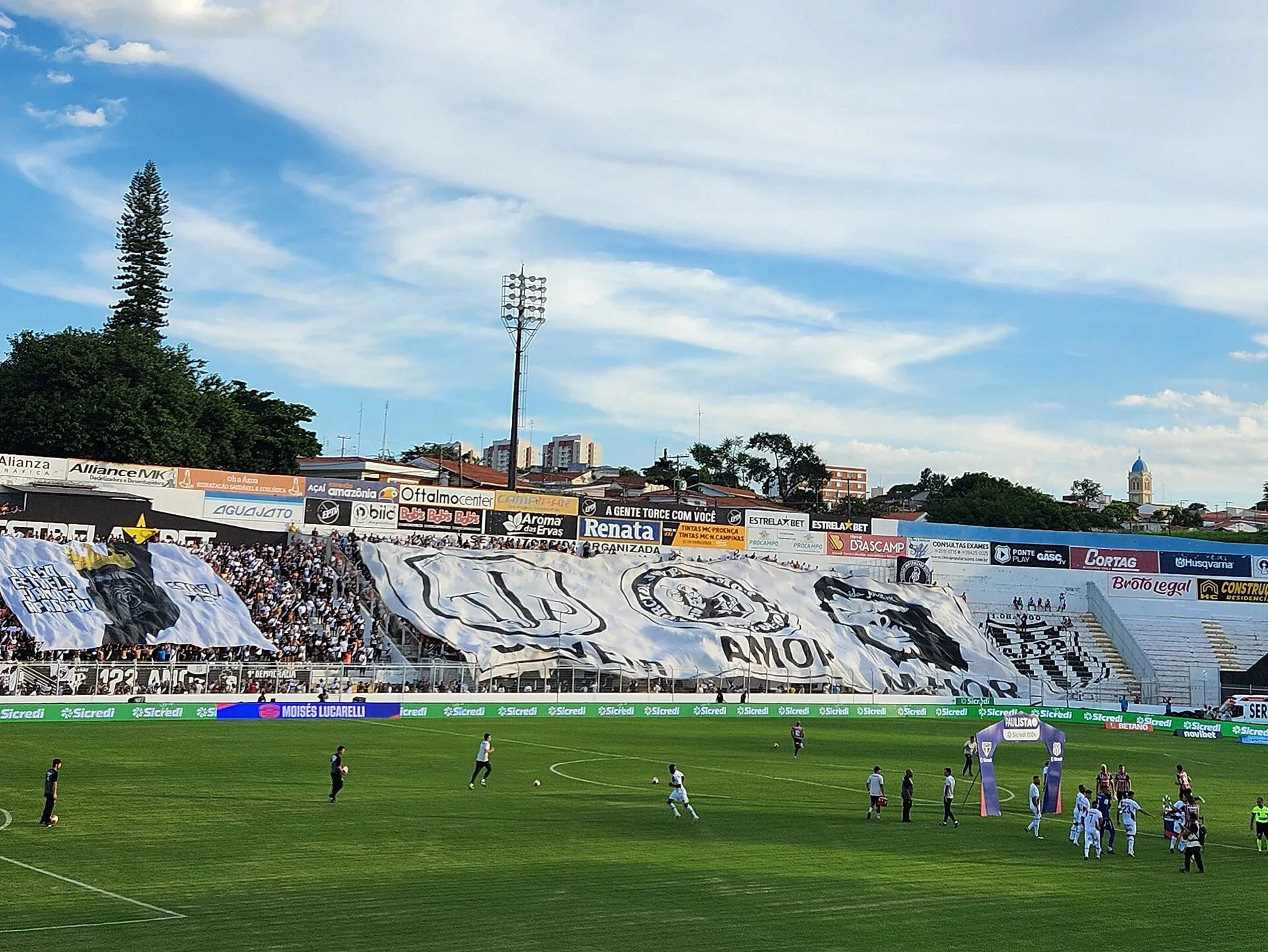 Estádio Moisés Lucarelli com campo de futebol, arquibancadas e céu azul