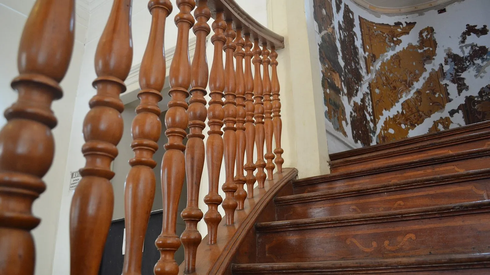 Escada de madeira com balaústres torneados e degraus marchetados no interior do Palácio dos Azulejos, com pintura antiga descascada na parede