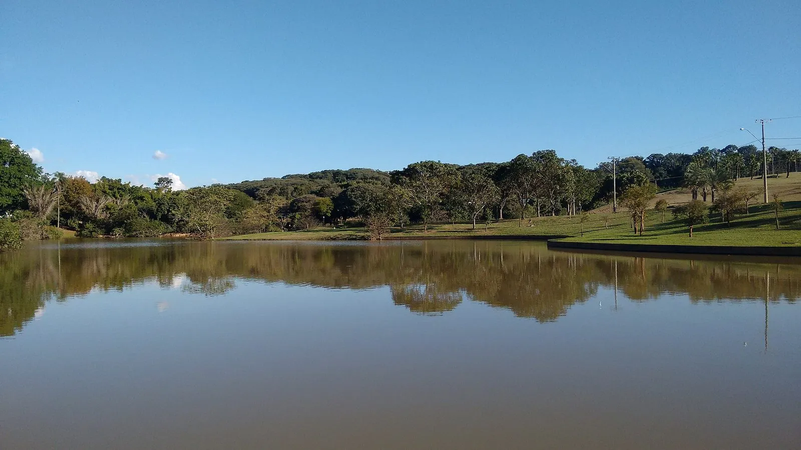 Lago do Parque Ecológico de Campinas em dia de céu azul, com árvores refletidas na água