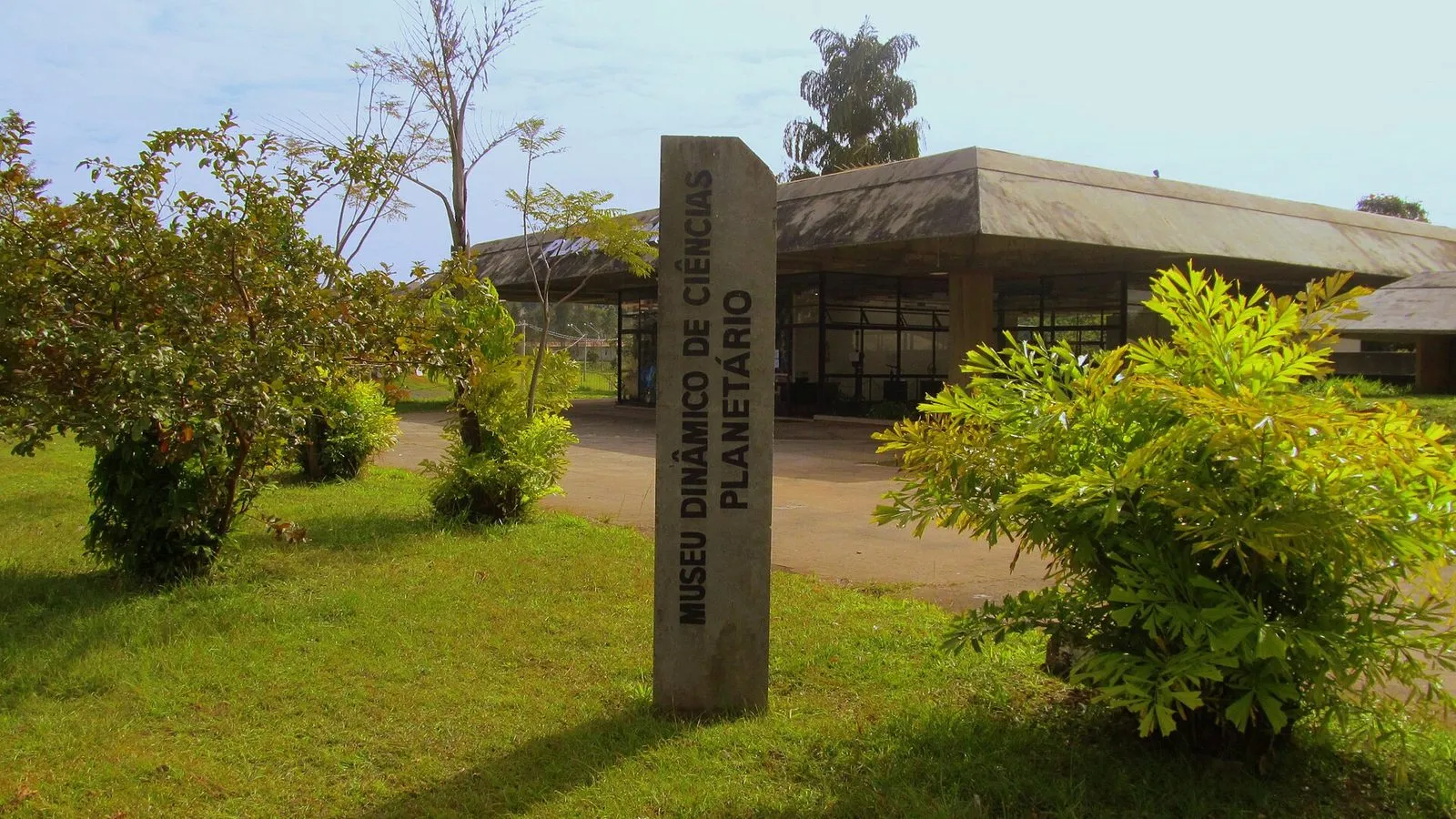 Marco de concreto com o nome Museu Dinâmico de Ciências e Planetário diante do prédio do museu, no Parque Portugal, em Campinas