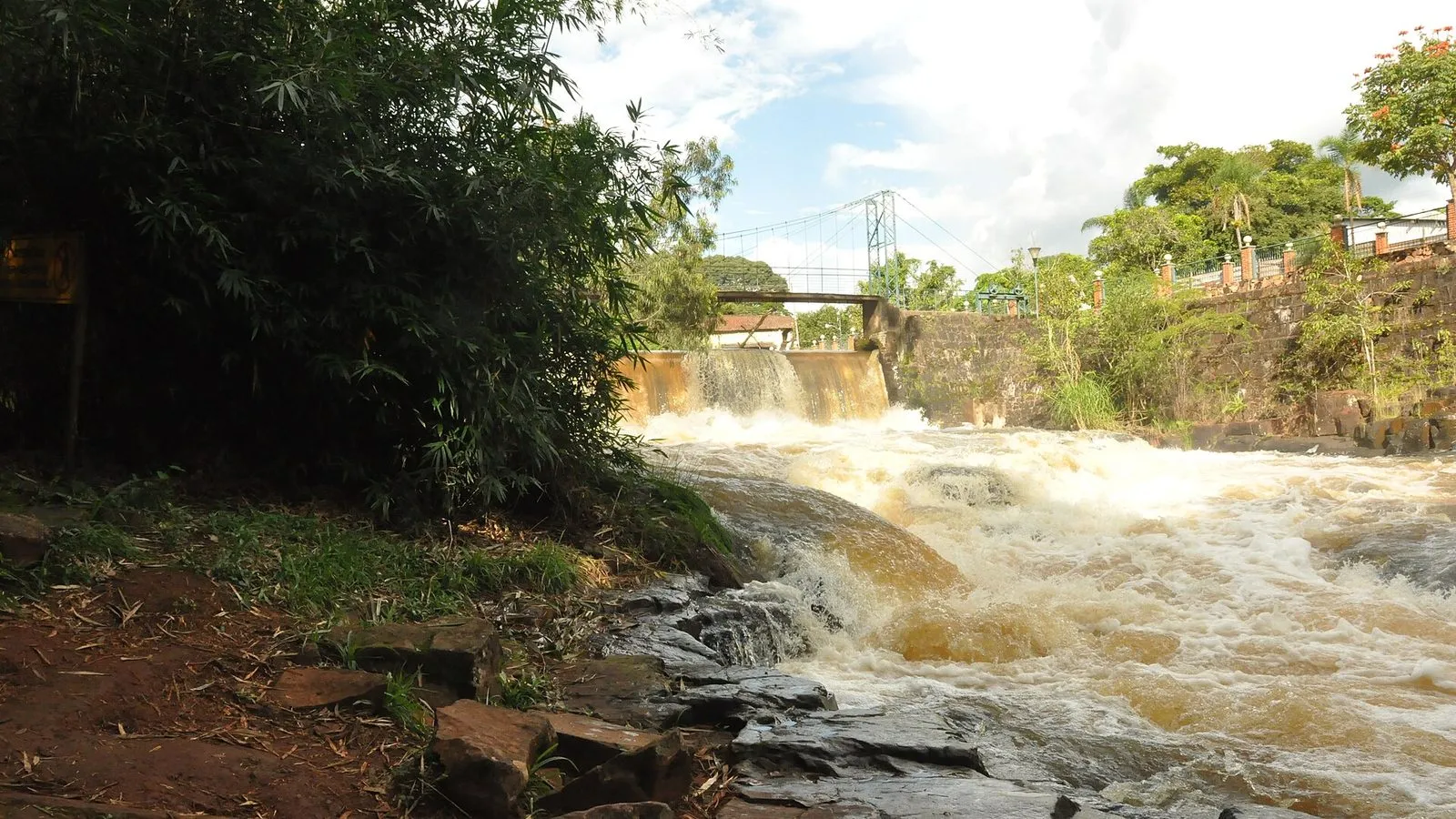 Queda d'água do Rio Jacaré-Pepira no Parque dos Saltos, em Brotas, com ponte pênsil ao fundo e mata na margem