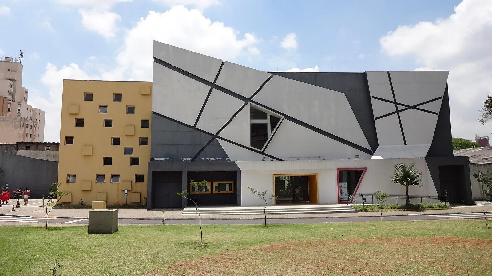 Fachada do Teatro Municipal Castro Mendes, em Campinas, com painéis geométricos cinza e prédio amarelo ao lado, em dia de céu azul